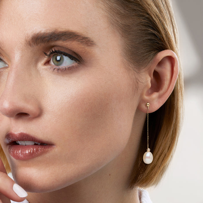 Cultured pearl drop earrings with yellow gold bead chain, worn on ear