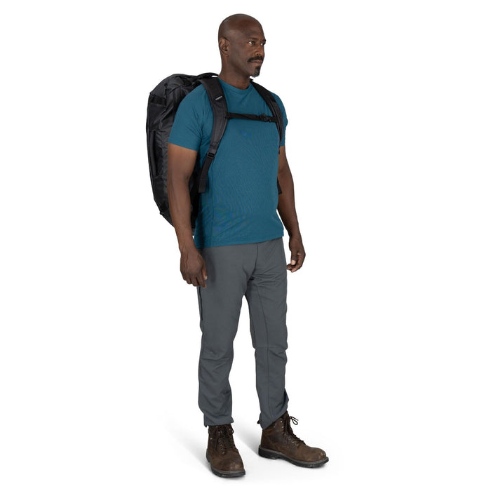 On-Body Front Carry – Male model wearing the Osprey Transporter Duffel 65 in Raven Black as a backpack with padded harness straps.