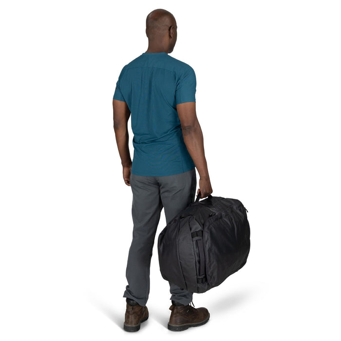 On-Body Side Carry (Back View) – Male model holding the Osprey Transporter Duffel 65 in Raven Black by its side handle.