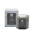 A gray octagonal glass Tarmac Candle by Antica Farmacista/Harper sits before its matching box, both with black and silver labels highlighting scents of silver woods, earthy oak, and green cedar.